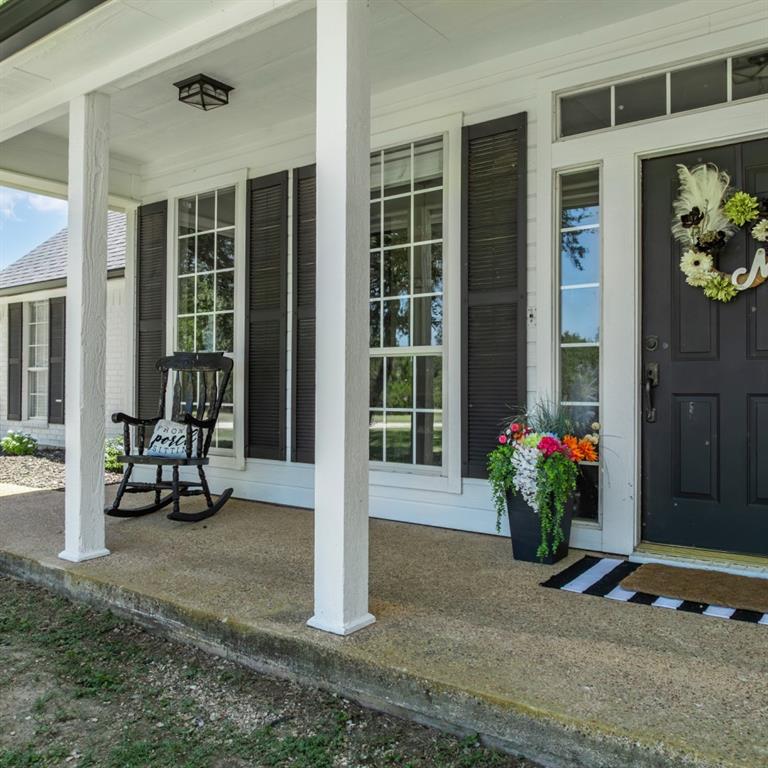 Covered front porch with a textured concrete surface, white support columns, and a dark entry door with sidelights and transom windows