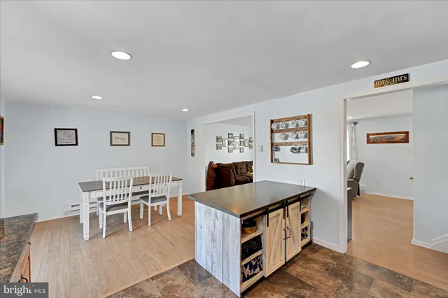a living room with stainless steel appliances kitchen island granite countertop a table chairs and a refrigerator
