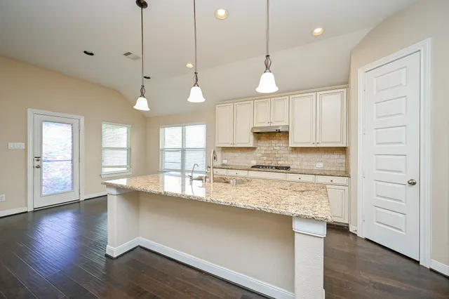 a large kitchen with granite countertop a stove a sink and a wooden floor