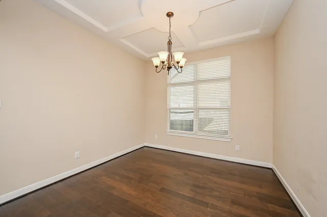an empty room with wooden floor chandelier and windows
