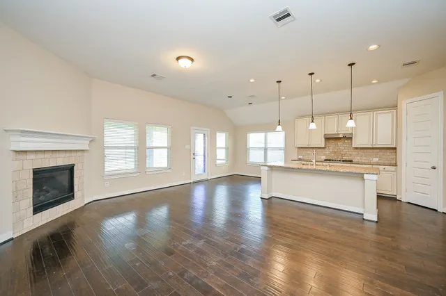 a view of an empty room with kitchen and fireplace