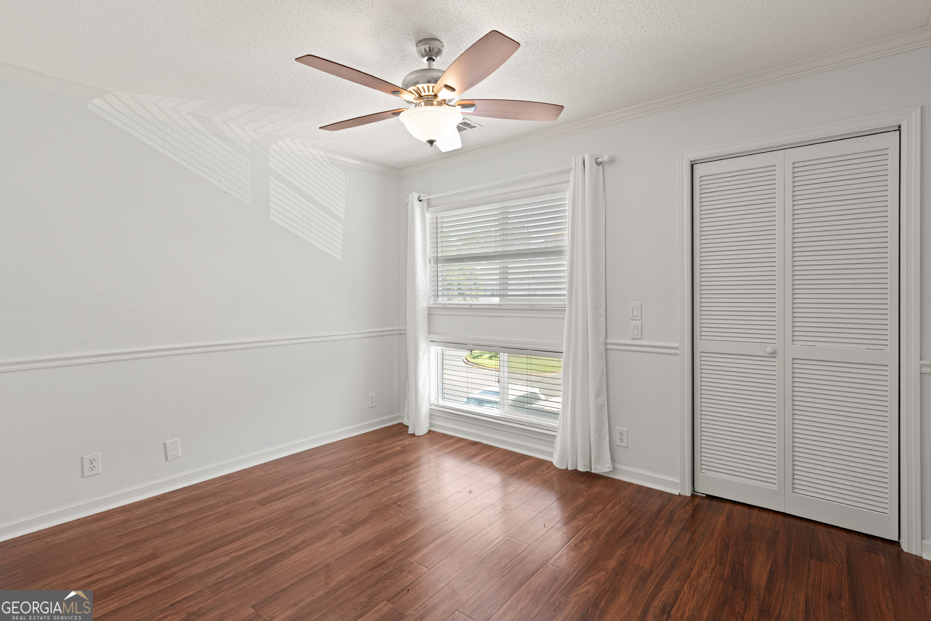 1000 Mallery St Extension, Unit B5 St. Simons, GA 31522 - Photo 21 of 24 an empty room with wooden floor chandelier fan and windows