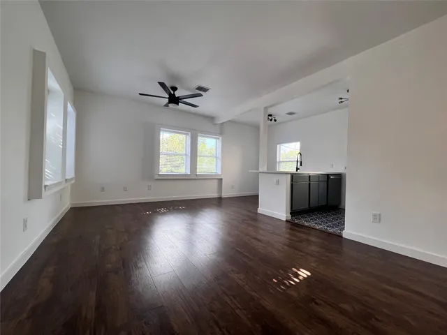 an empty room with wooden floor a ceiling fan and windows