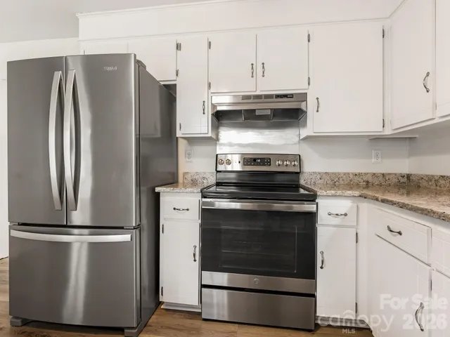 a kitchen with stainless steel appliances granite countertop a refrigerator stove and white cabinets