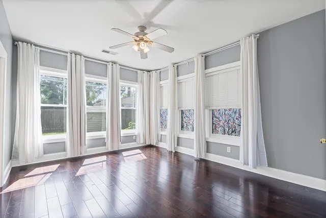 a view of an empty room with wooden floor and fan