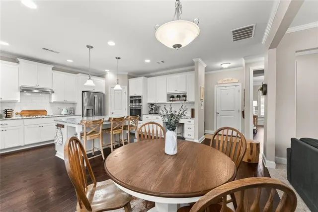 a kitchen with stainless steel appliances granite countertop a stove top oven a sink a refrigerator and white cabinets with wooden floor