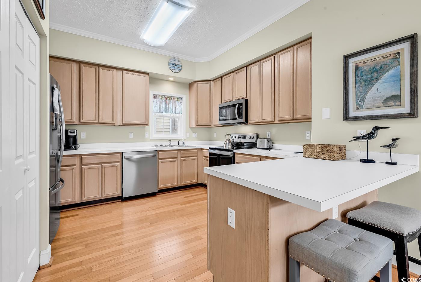 17 South Oak Drive Surfside Beach, SC 29575 - Photo 2 of 38 Kitchen with stainless steel appliances, a peninsula, a breakfast bar, a textured ceiling, and light brown cabinets