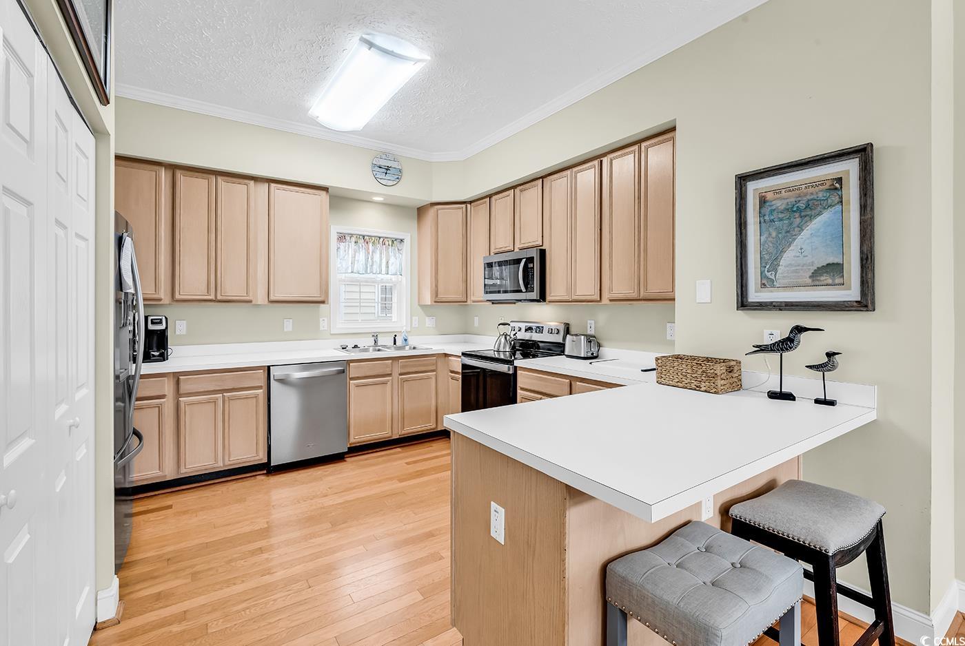 17 South Oak Drive Surfside Beach, SC 29575 - Photo 3 of 38 Kitchen featuring stainless steel appliances, a peninsula, a kitchen bar, light brown cabinets, and a textured ceiling