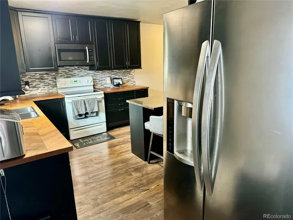 a kitchen with stainless steel appliances granite countertop a refrigerator a stove and a sink with wooden floor