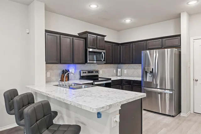 a kitchen with granite countertop a refrigerator a sink a stove a microwave and wooden cabinets