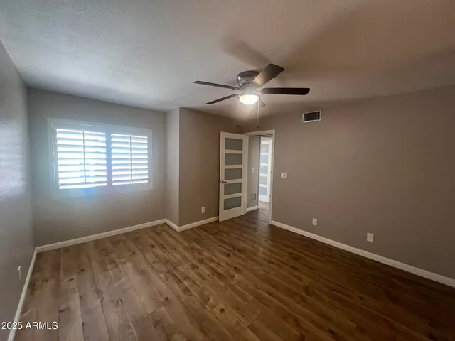 an empty room with wooden floor chandelier fan and windows