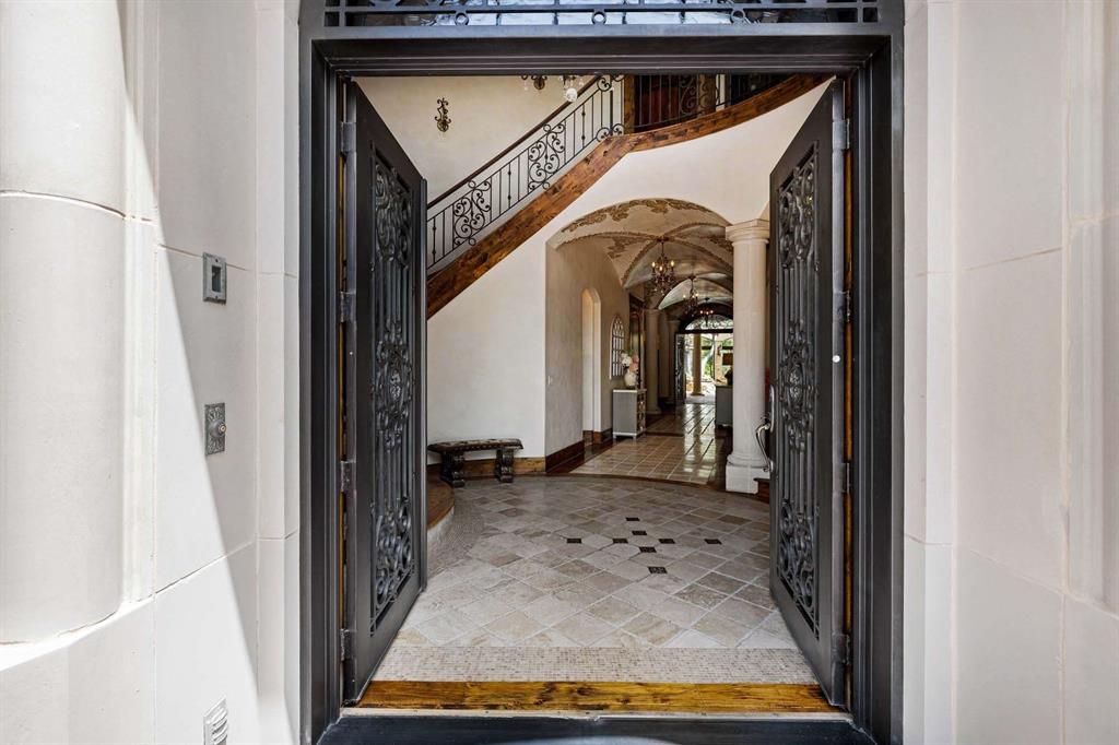 2115 Paradise Rnch Trail McKinney, TX 75071 - Photo 4 of 40 Grand entryway featuring ornate double doors, stone tile flooring with a patterned inlay, a curved staircase with a dark wrought iron railing, vaulted ceilings with decorative accents, and a hallway extending into the interior