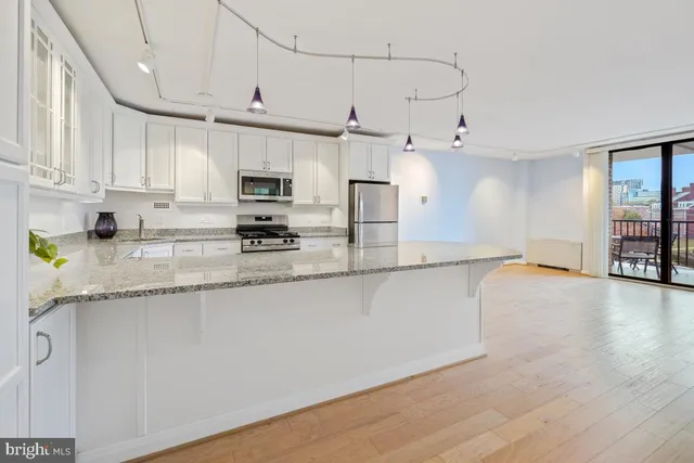 a kitchen with granite countertop a stove a sink and white cabinets with wooden floor