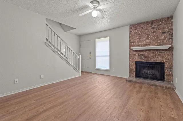 a view of an empty room with wooden floor fireplace and a window
