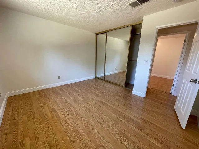 a view of an empty room with wooden floor and a mirror