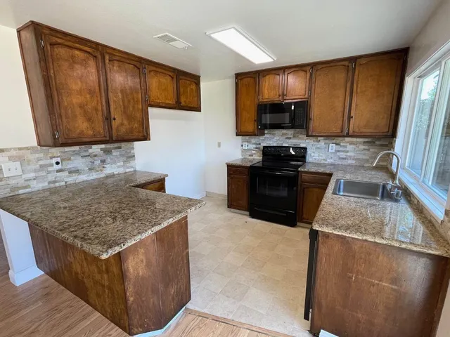 a kitchen with granite countertop a sink a stove top oven a refrigerator cabinets and wooden floor