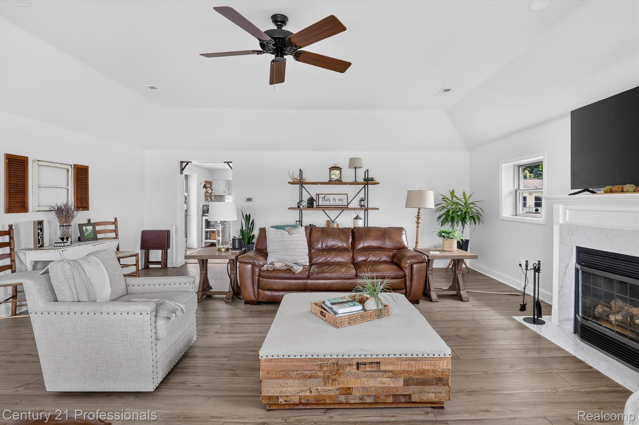 13525 Dennison Road Milan, MI 48160 - Photo 12 of 69 Spacious living area featuring vaulted ceilings with a ceiling fan, wood-finish flooring, and a fireplace with a white mantel and light-toned surround