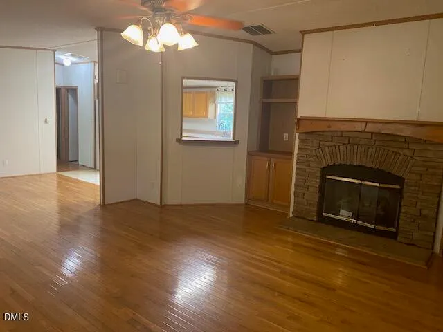 a view of an empty room with wooden floor fireplace and a window
