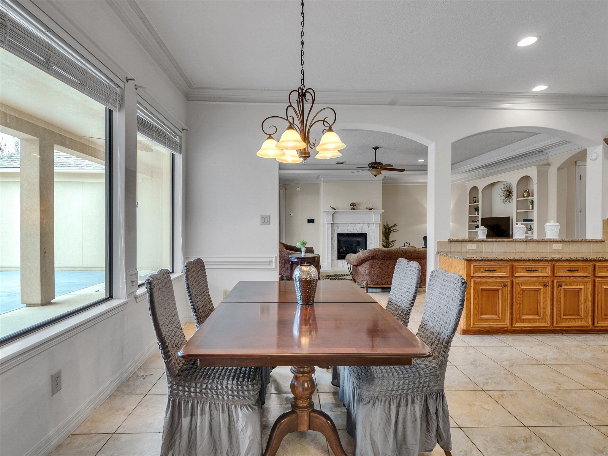 6914 Sandwedge Point Court Spring, TX 77389 - Photo 22 of 50 This spacious, well-lit dining area features large windows with views of the patio. It opens into a cozy living room with a fireplace and built-in shelving. The adjacent kitchen has a granite countertop island and wooden cabinetry, creating a warm, inviting atmosphere.
