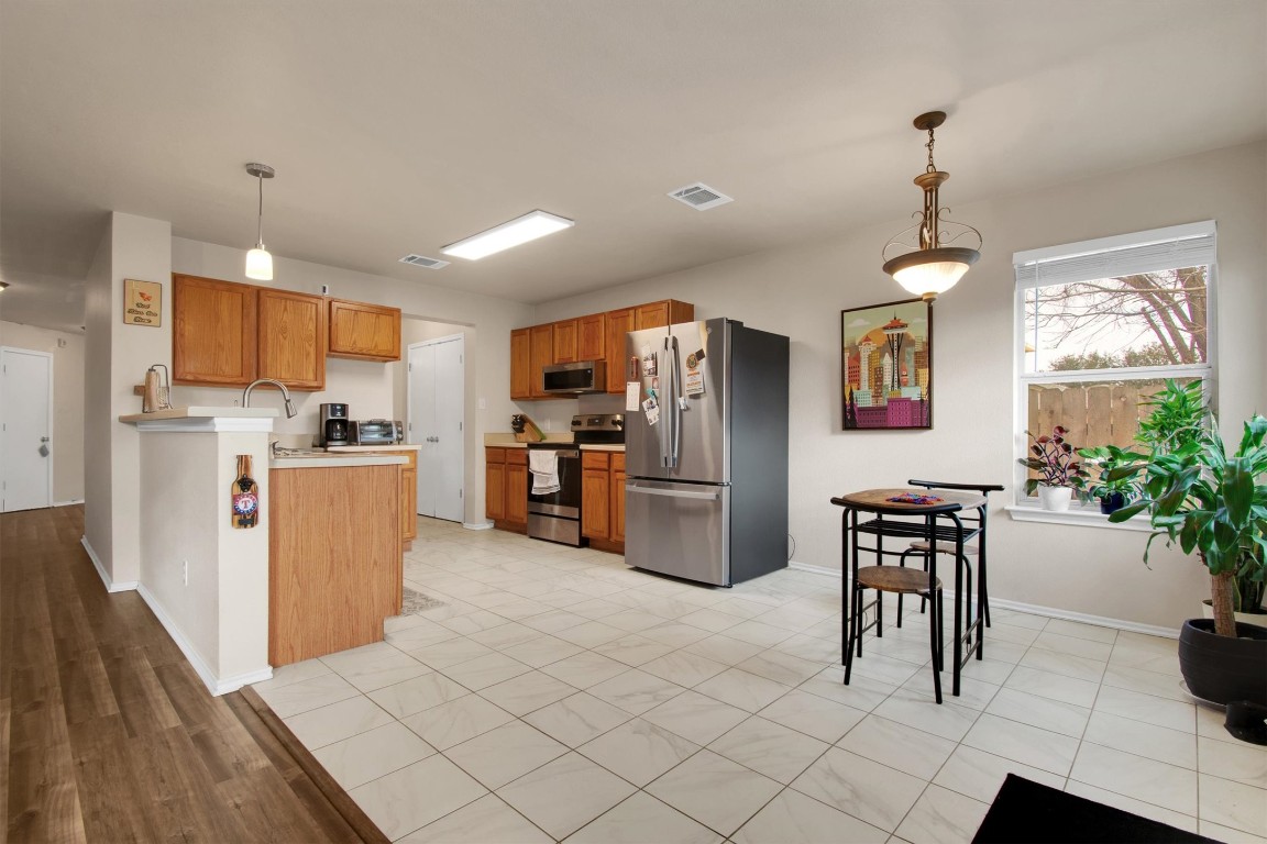 18205 Topsail Street Manor, TX 78653 - Photo 10 of 29 Kitchen with stainless steel appliances, light countertops, brown cabinetry, decorative light fixtures, and a peninsula
