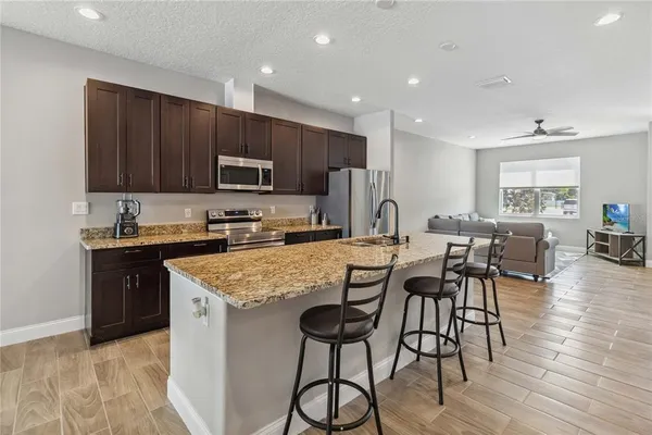 a kitchen with stainless steel appliances granite countertop wooden cabinets a refrigerator a stove a sink and a oven with wooden floor