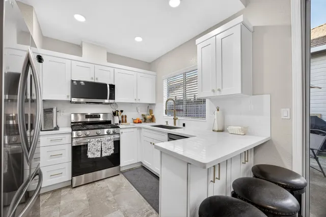 a kitchen with stainless steel appliances granite countertop a dining table chairs refrigerator and sink