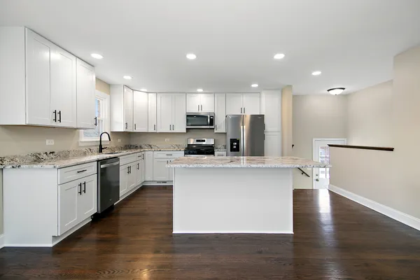 a kitchen with stainless steel appliances granite countertop a sink a stove a refrigerator and white cabinets