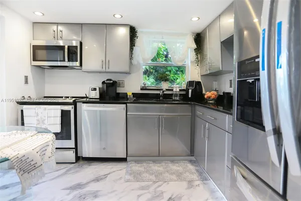 a kitchen with stainless steel appliances a sink a stove a microwave a refrigerator a sink a window and cabinets