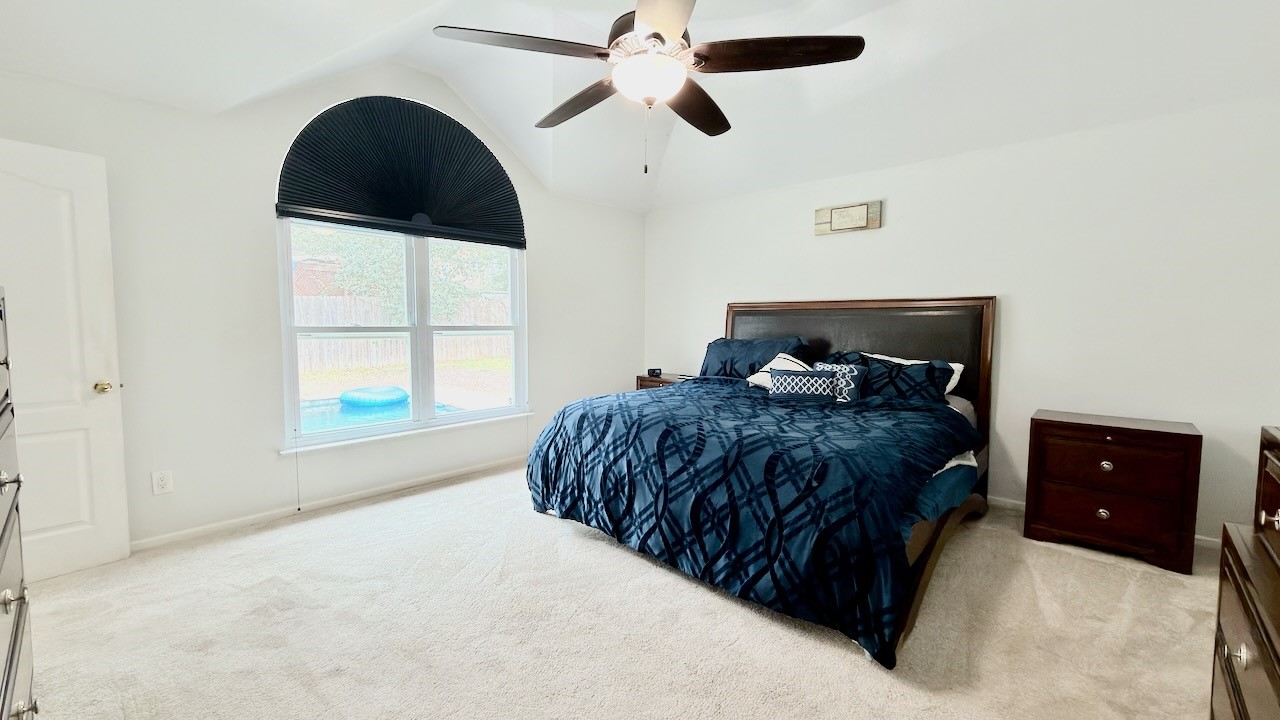 1902 Overland Drive Leander, TX 78641 - Photo 14 of 29 Tucked quietly at the back of the home, the primary suite offers a true sense of separation from the guest bedrooms, creating a peaceful and private retreat. Oversized windows frame calming views of the backyard, bringing in natural light while keeping the space connected to the outdoors. A generous walk-in closet adds everyday functionality, and custom blackout shades in the bedroom provide ideal light control for restful mornings and relaxed evenings.