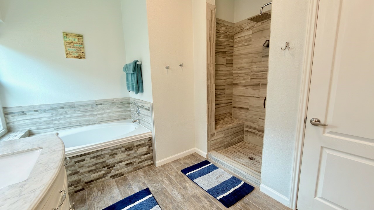 1902 Overland Drive Leander, TX 78641 - Photo 17 of 29 Step into a refreshed primary bathroom designed for both comfort and everyday ease. Dual vanities provide plenty of space for morning routines, while the separate shower and soaking tub create a flexible layout that works for busy days and slower evenings alike. Recent updates include tile flooring underfoot, a fully tiled shower with rain shower head, and upgraded tile surrounds around the bathtub, bringing a clean, modern look that feels both polished and practical.