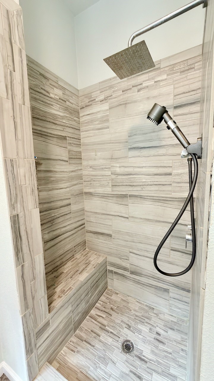 1902 Overland Drive Leander, TX 78641 - Photo 18 of 29 Step into a refreshed primary bathroom designed for both comfort and everyday ease. Dual vanities provide plenty of space for morning routines, while the separate shower and soaking tub create a flexible layout that works for busy days and slower evenings alike. Recent updates include tile flooring underfoot, a fully tiled shower with rain shower head, and upgraded tile surrounds around the bathtub, bringing a clean, modern look that feels both polished and practical.
