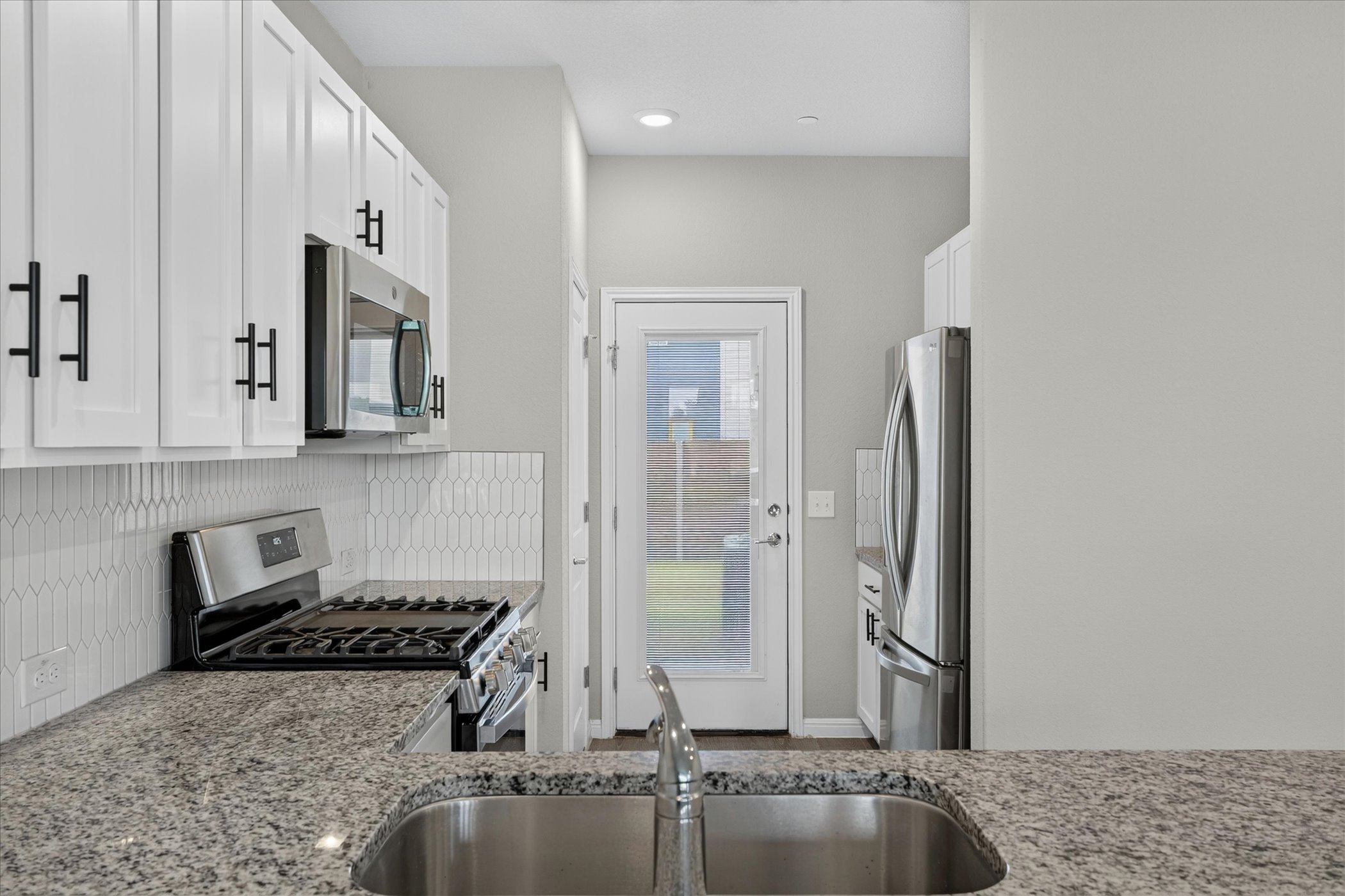 9015 Cattle Baron Path, Unit 1102 Austin, TX 78747 - Photo 6 of 25 A well-lit kitchen features granite countertops, stainless steel appliances, and a convenient rear entry.