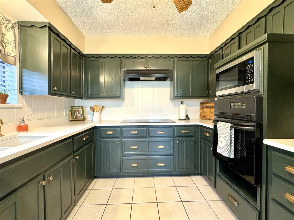 113 Northeast Timber Ridge Drive Burleson, TX 76028 - Photo 14 of 36 MAGNOLIA Inspired dark green kitchen cabinetry, white QUARTZ countertops, smooth glass electric COOKTOP, beadboard backsplash, tile flooring, and integrated appliances.