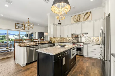 a kitchen with granite countertop a refrigerator sink stove and white cabinets