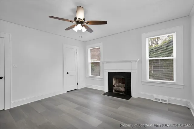 a view of an empty room with wooden floor fireplace and a window