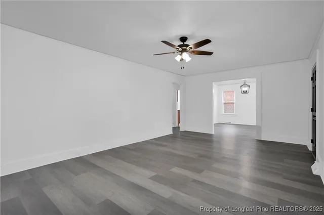 a view of an empty room with wooden floor and a ceiling fan