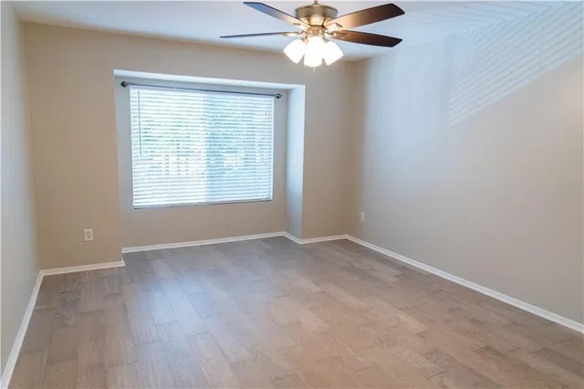 an empty room with wooden floor fan and windows