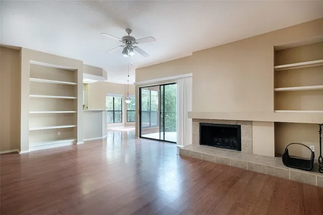 a view of an empty room with wooden floor fireplace and a window