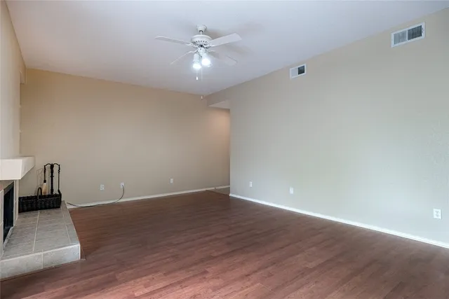 a view of an empty room with wooden floor and a ceiling fan