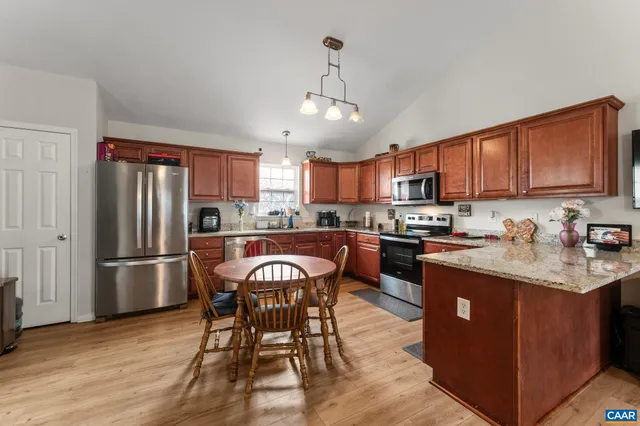 a kitchen with stainless steel appliances granite countertop a stove top oven a refrigerator a sink a dining table and chairs with wooden floor