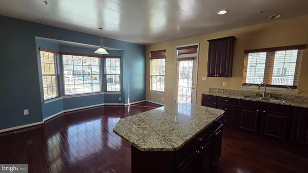 a kitchen with kitchen island granite countertop wooden cabinets a refrigerator a stove a sink and dishwasher with wooden floor