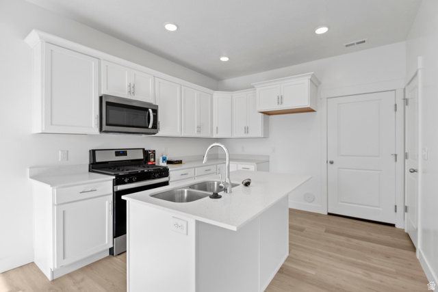 1271 West 500 South Logan, UT 84321 - Photo 6 of 26 Modern kitchen featuring an island with a double basin sink, white cabinetry with crown molding, stainless steel appliances, recessed lighting, and wood-finish flooring