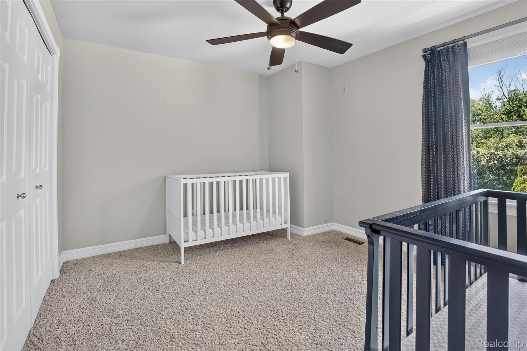 7186 East River Road Flushing, MI 48433 - Photo 19 of 47 Neutral-toned wall paint with a ceiling fan light fixture, light-colored carpet flooring, a window with drapery, and white bi-fold closet doors