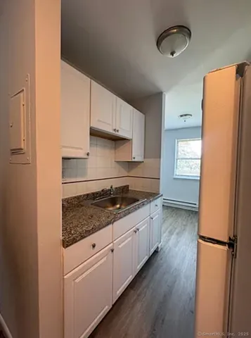 a kitchen with granite countertop a refrigerator a sink dishwasher a stove and white countertops with wooden floor