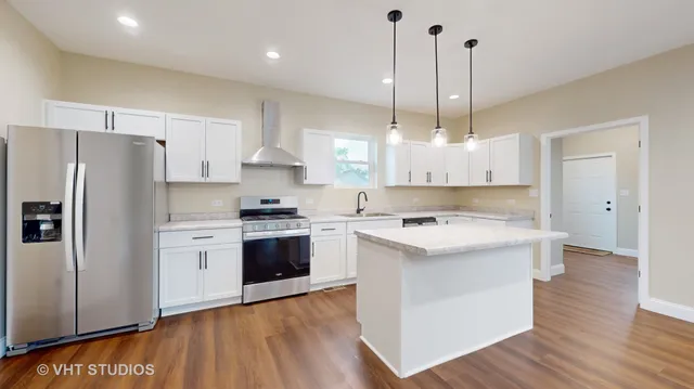 a kitchen with kitchen island a sink a stove a refrigerator and white cabinets with wooden floor