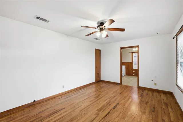 a view of an empty room with wooden floor and a ceiling fan