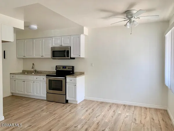 a kitchen with granite countertop a stove top oven a sink and dishwasher with white cabinets