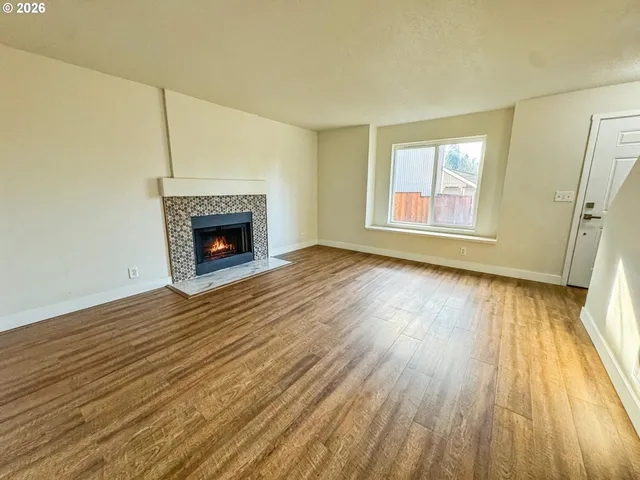 an empty room with wooden floor fireplace and windows