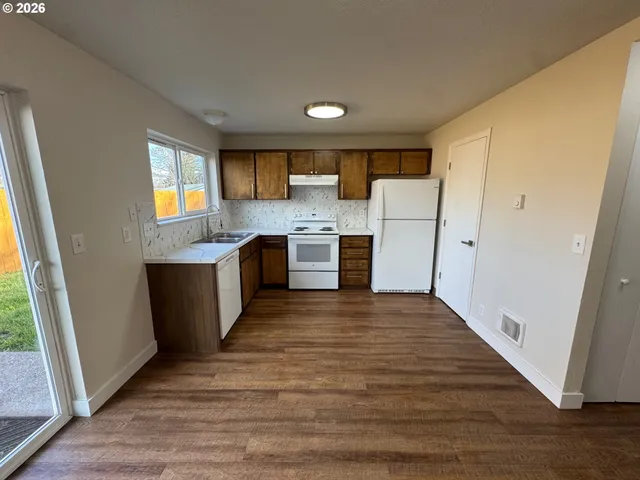 a large kitchen with a stove a refrigerator a sink dishwasher and wooden cabinets with wooden floor