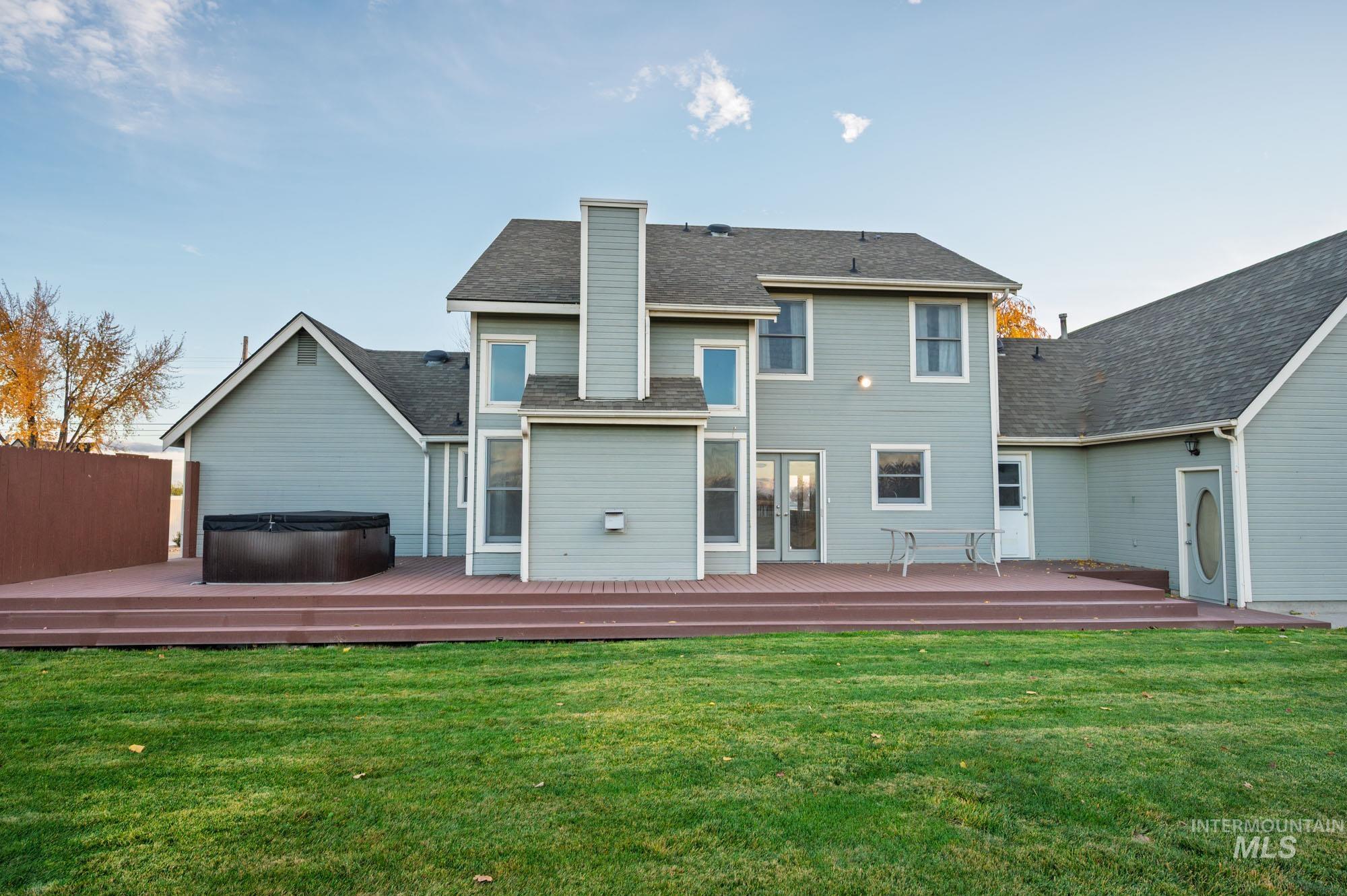 7790 Ustick Road Nampa, ID 83687 - Photo 29 of 41 Back of property with a hot tub, a wooden deck, a shingled roof, and a chimney